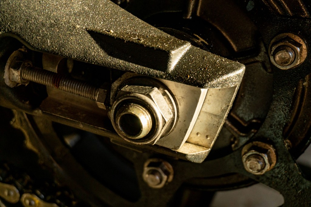 A close-up of a 2012 Triumph Street Triple R axle nut and chain adjuster with reference marks