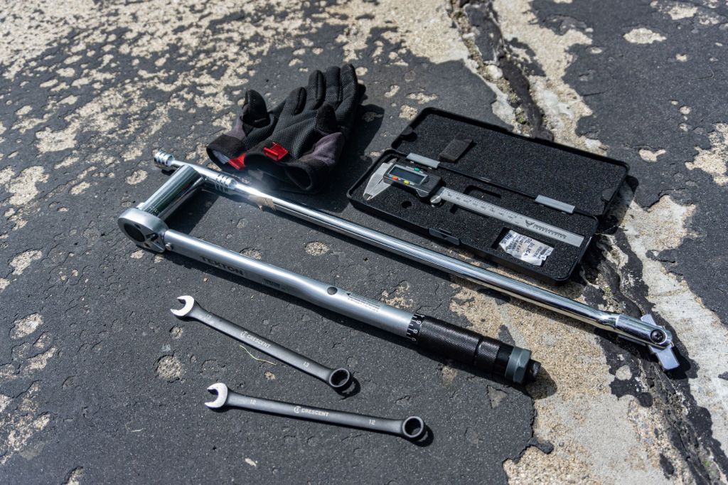 Digital calipers, a torque wrench, open-end wrenches, and mechanic gloves used to adjust the chain slack on a 2012 Triumph Street Triple R motorcycle