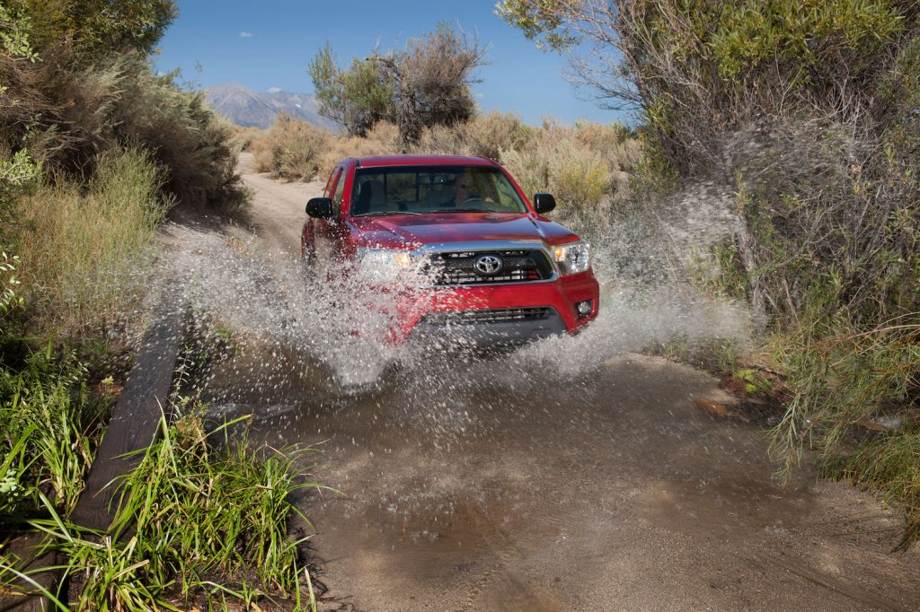 A red 2013 Toyota Tacoma driving through water