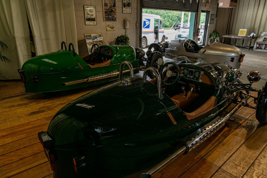 Two green 2013 Morgan 3-Wheelers in front of a silver 2012 Morgan 3-Wheeler in a garage