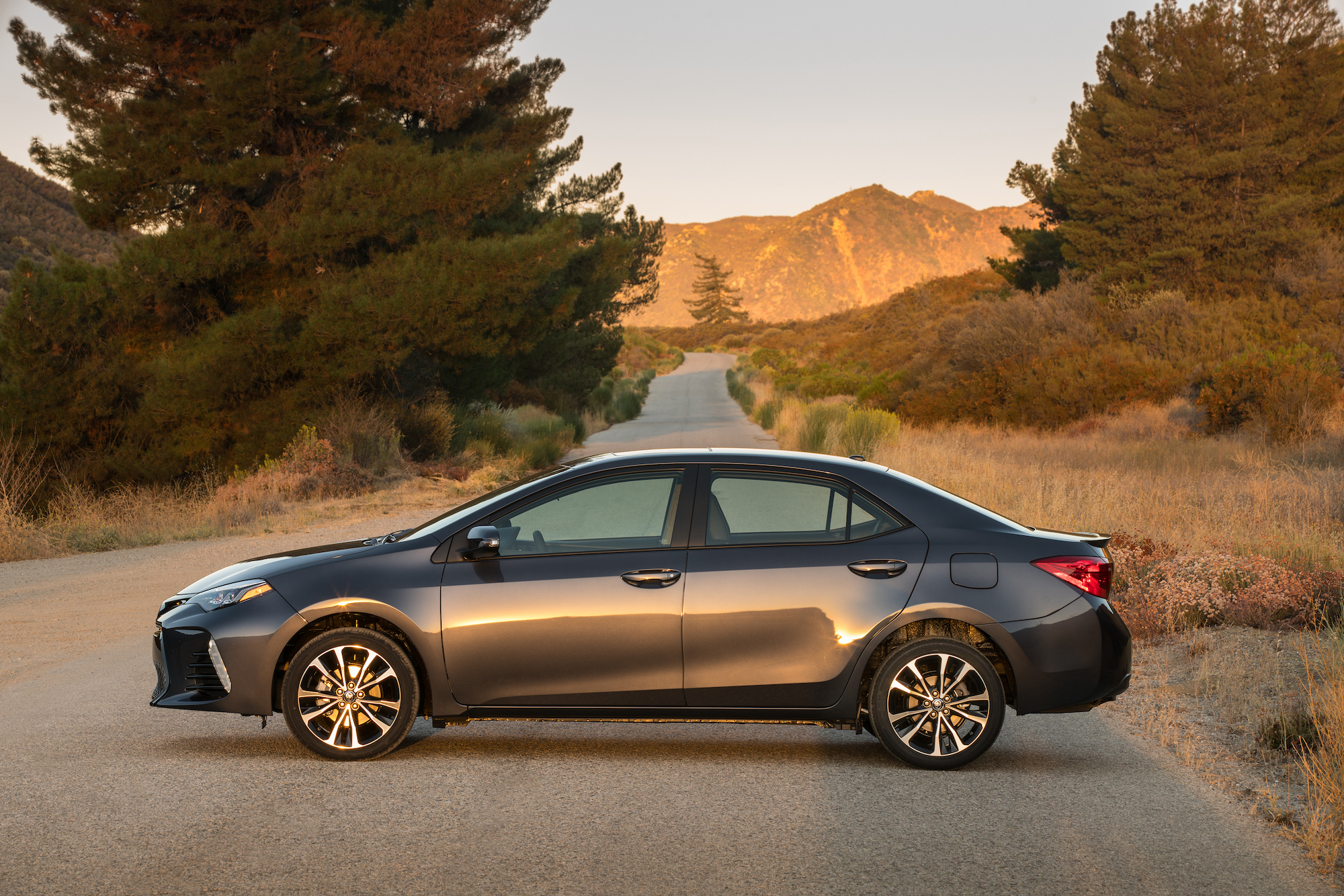 A dark gray metallic 2018 Toyota Corolla XSE parked on a country road surrounded by pine trees and mountains