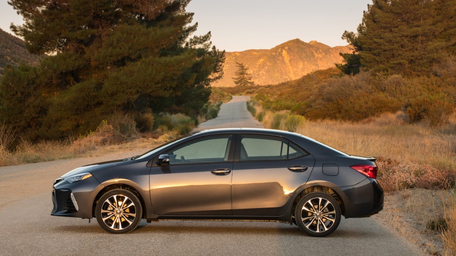 A dark gray metallic 2018 Toyota Corolla XSE parked on a country road surrounded by pine trees and mountains