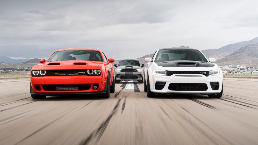 A red 2020 Dodge Challenger SRT Super Stock and a 2021 Charger SRT Hellcat Redeye race next to each other on a track with a 2021 Durango SRT Hellcat in the background