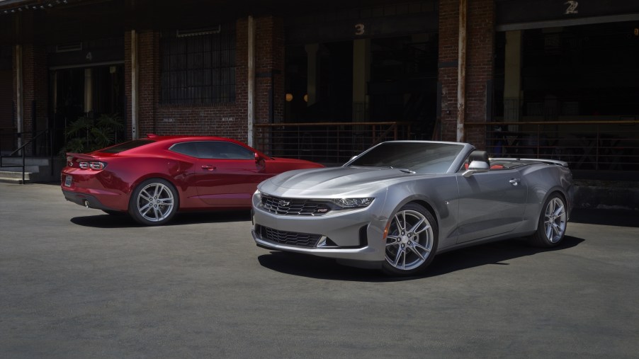 A red 2021 Chevy Camaro LS and a silver 2021 Camaro LT parked next to each other outside an old brick building