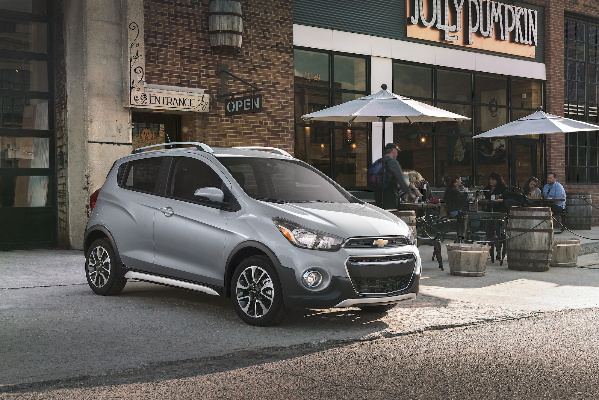 A silver 2021 Chevy Spark three-door hatchback parked outside a Jolly Pumpkin bakery and café