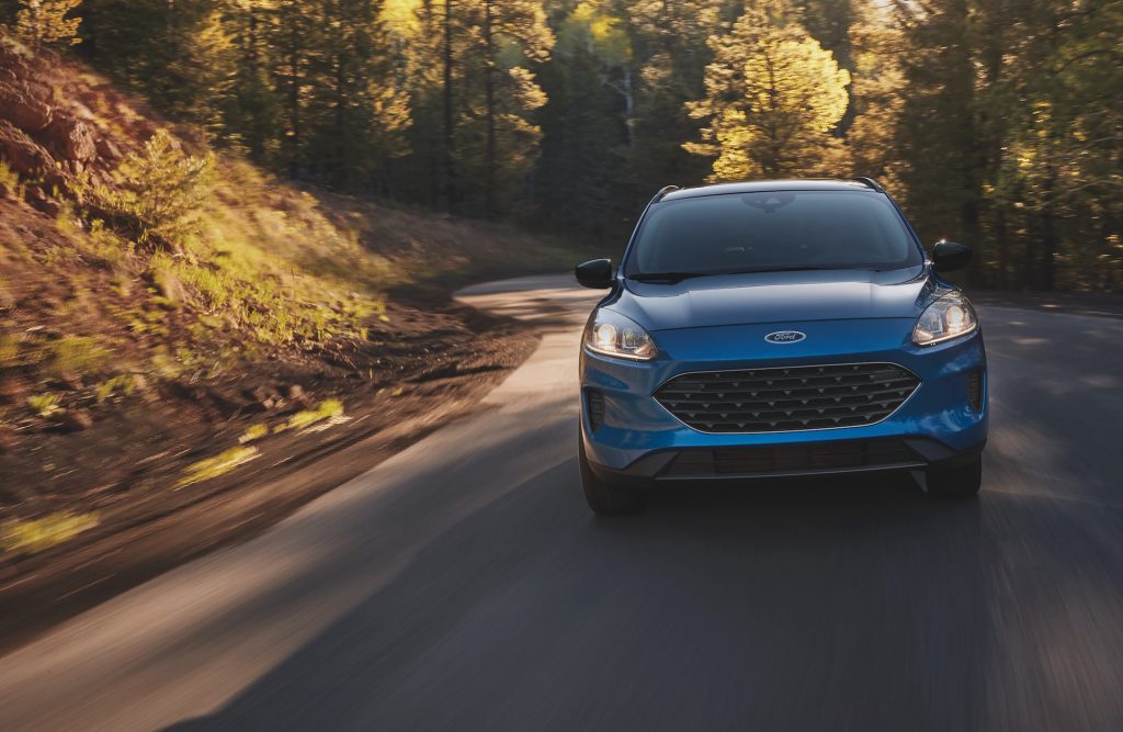 A blue metallic 2021 Ford Escape compact SUV travels on a tree-lined, sun-dappled country road