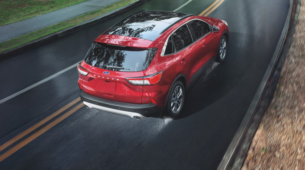 A red 2021 Ford Escape travels on a wet two-lane highway. The Ford Escape hybrid is one of five SUVs with the best gas mileage, according to CarGurus.