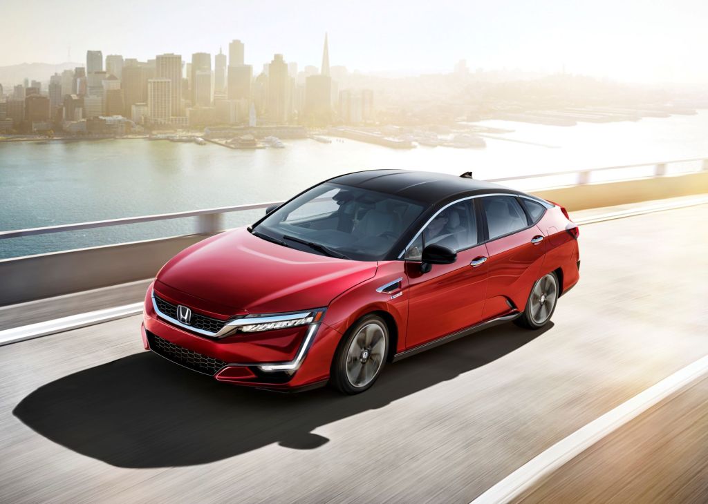 A red 2021 Honda Clarity Fuel Cell driving on a highway with an urban city in the background