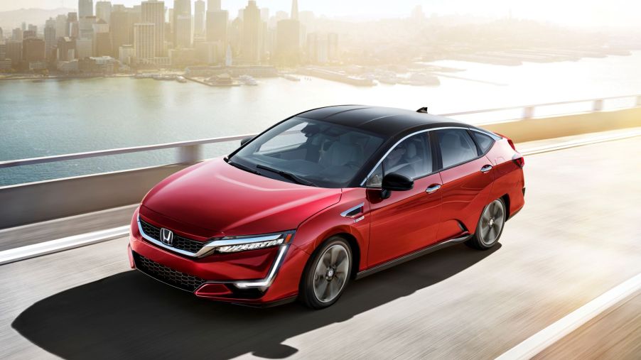 A red 2021 Honda Clarity Fuel Cell driving on a highway with an urban city in the background