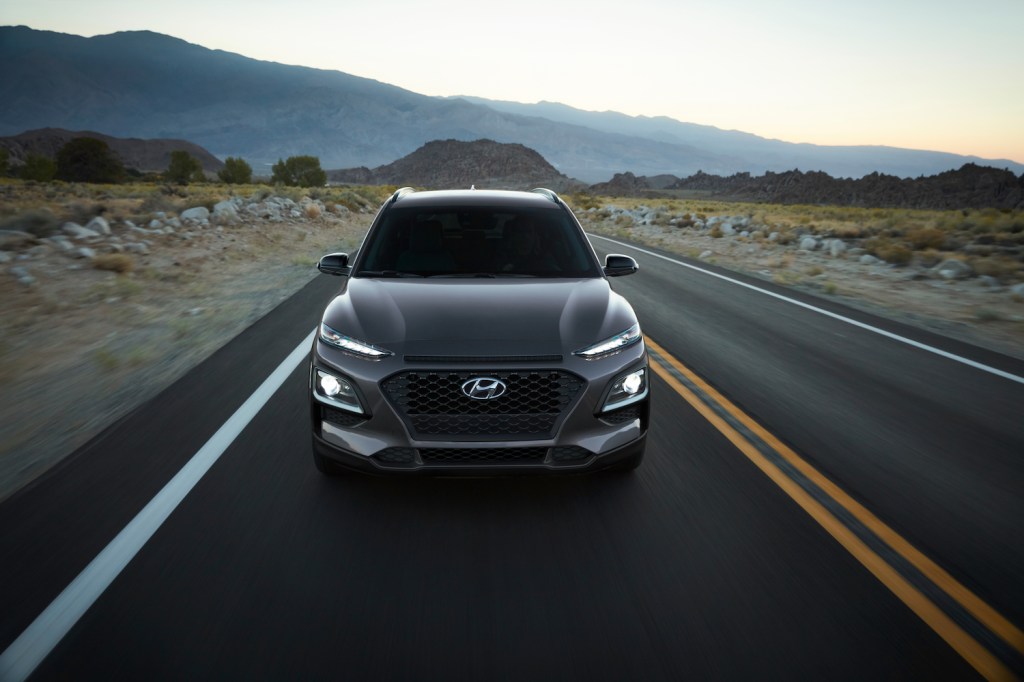 A grey 2021 Hyundai Kona EV driving on an empty road in the mountains