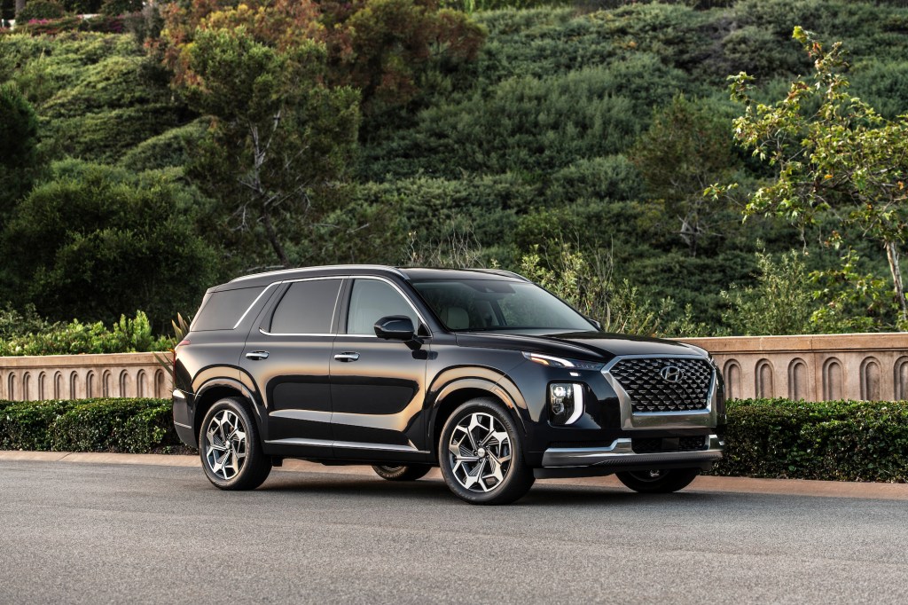 A black 2021 Hyundai Palisade midsize SUV parked along a concrete wall and shrubs on a hilllside