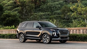 A black 2021 Hyundai Palisade midsize SUV parked along a concrete wall and shrubs on a hilllside