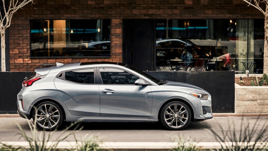 A silver 2021 Hyundai Veloster parked in front of a storefront