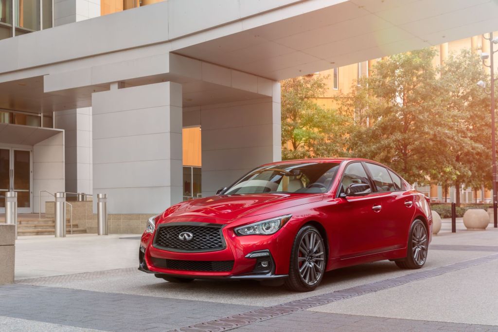 A red 2021 Infiniti Q50 sitting next to a modern style building in a wooded area.