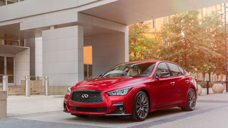A red 2021 Infiniti Q50 sitting next to a modern style building in a wooded area.