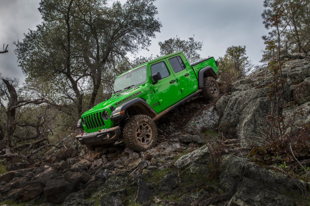 A 2021 Jeep Gladiator Rubicon in Gecko Green parked on the edge of a rocky incline on a cloudy day