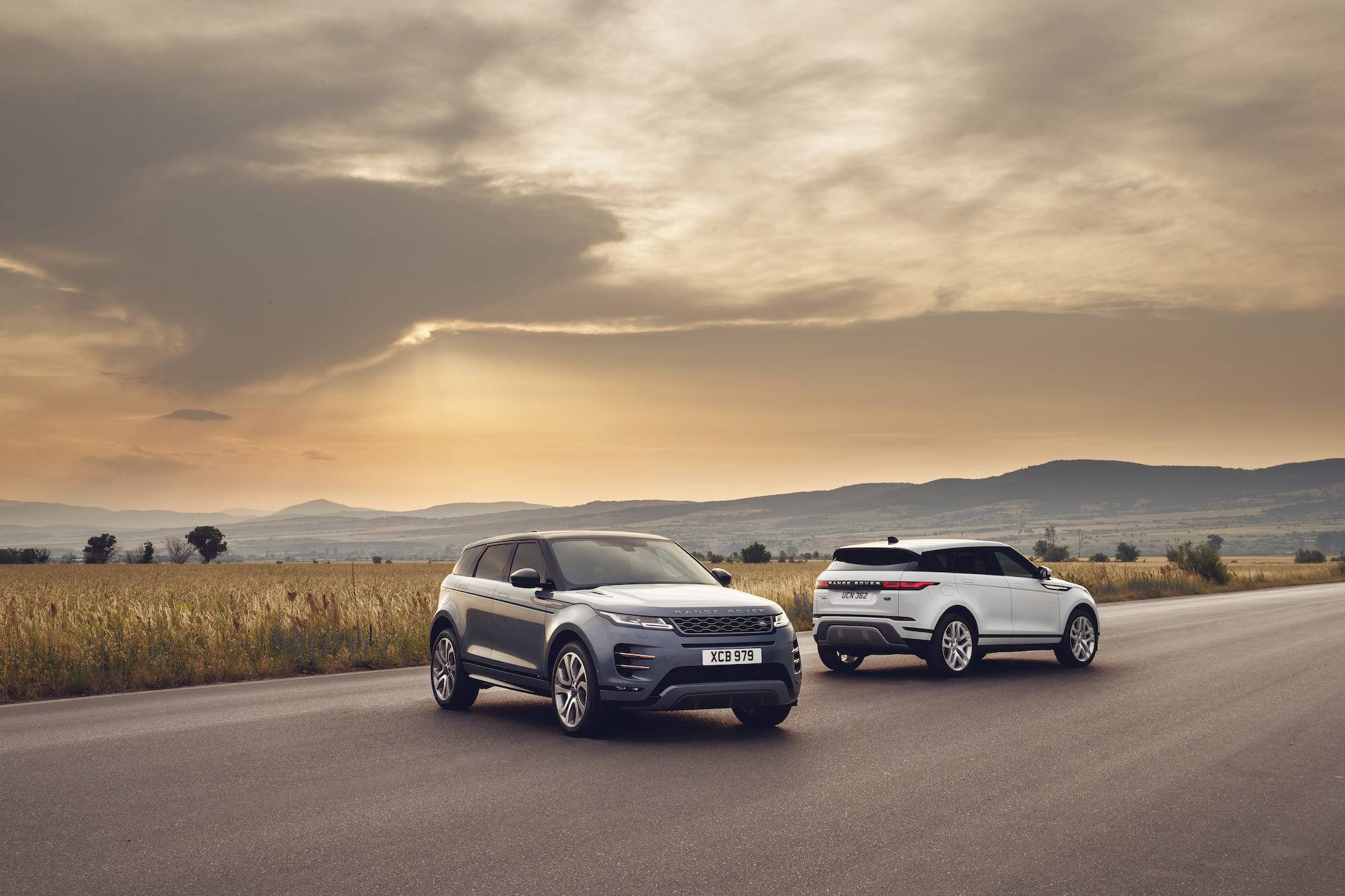 Two 2021 Land Rover Range Rover Evoque luxury compact SUVs parked on a road through a plain in front of mountains