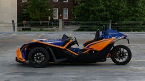 The side view of a blue-and-orange 2021 Polaris Slingshot R in a parking lot