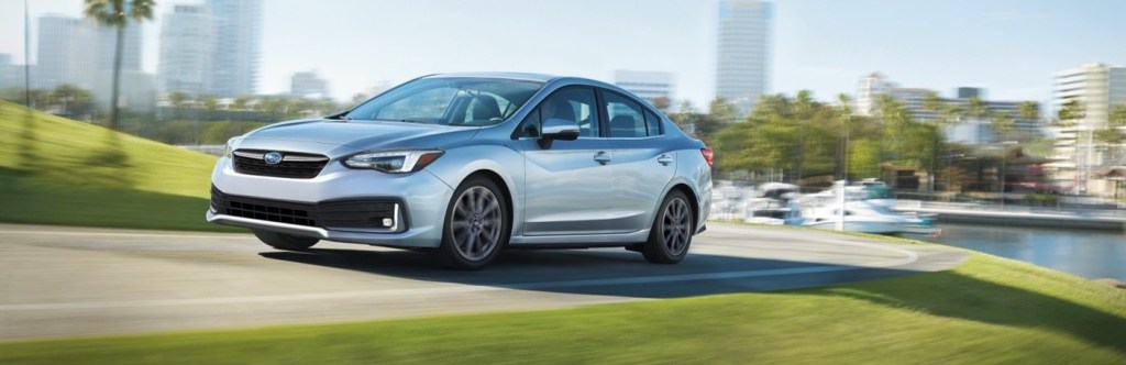 The 2021 Subaru Impreza sedan model in silver gray driving on the outskirts of a tropical city