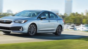 The 2021 Subaru Impreza sedan model in silver gray driving on the outskirts of a tropical city