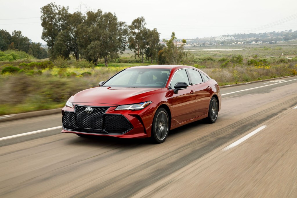 A red 2021 Toyota Avalon driving along a tree lined highway
