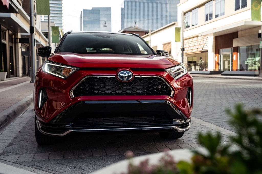 A red metallic 2021 Toyota RAV4 Prime XSE plug-in hybrid compact SUV parked on a brick road in a city