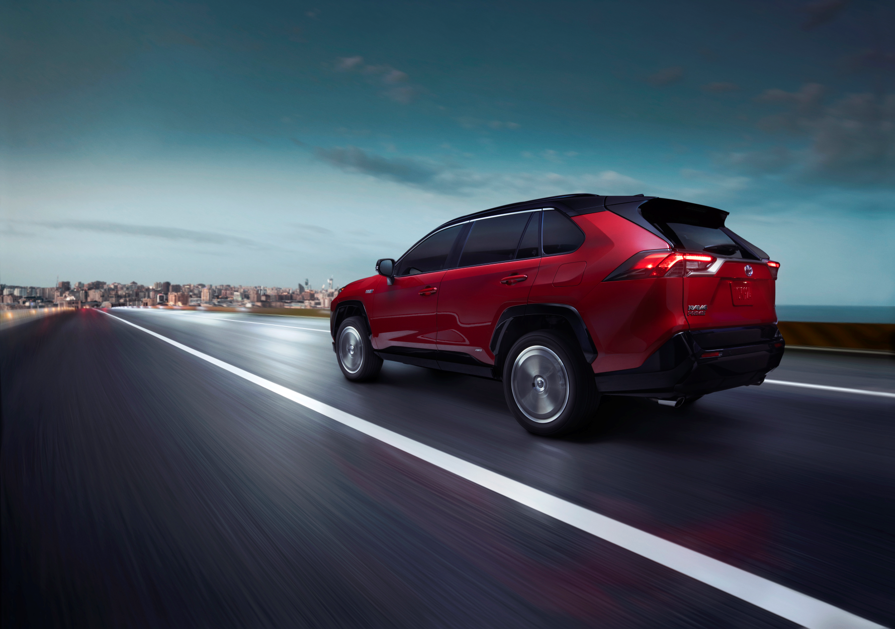 The 2021 Toyota RAV4 Prime PHEV SUV in dark red driving down a highway toward an urban city