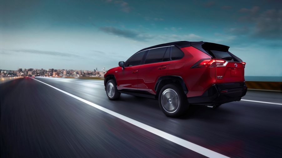The 2021 Toyota RAV4 Prime PHEV SUV in dark red driving down a highway toward an urban city
