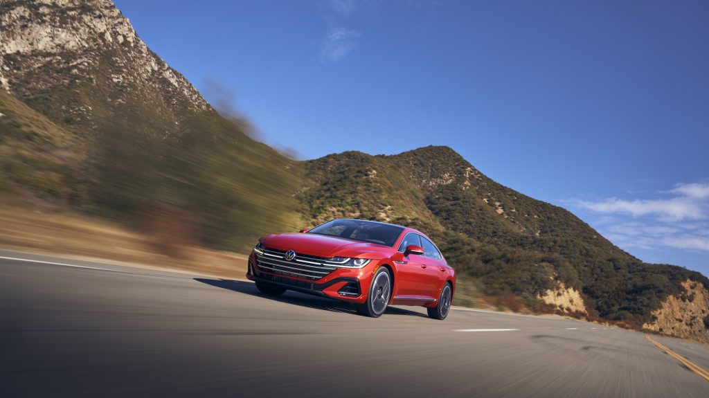 A red 2021 Volkswagen Arteon travels on a highway through mountains