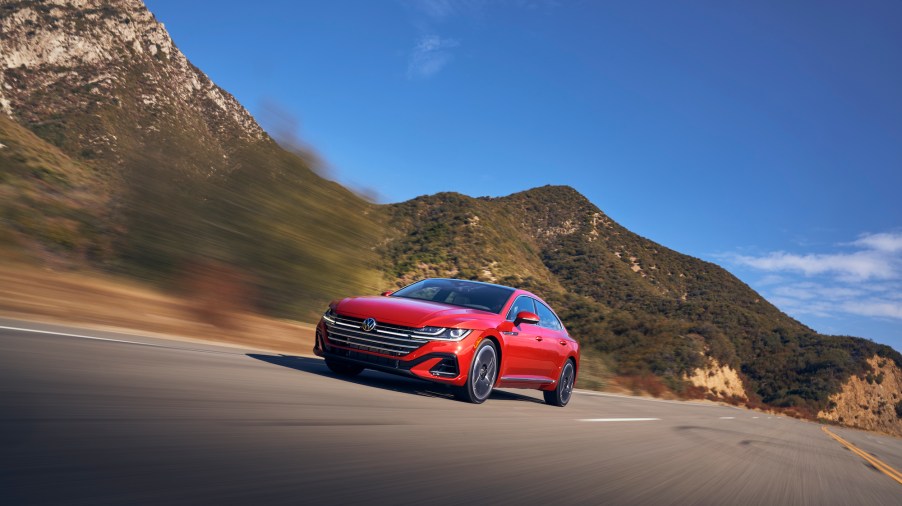 A red 2021 Volkswagen Arteon travels on a highway through mountains