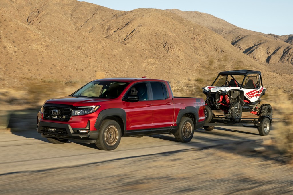 This is a publicity photo of a red 2021 Ridgeline Sport with HPD Package towing a side-by-side. The Ridgeline is one of the true compact trucks on the market.