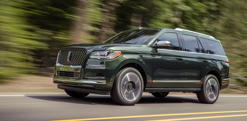 A 2022 Lincoln Navigator Manhattan Green Black Label traveling on a two-lane highway passing a blur of trees