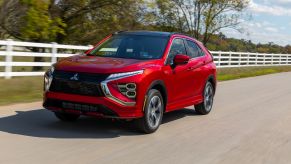 A red 2022 Mitsubishi Eclipse Cross compact SUV model driving by a white fence