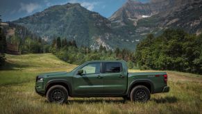 The 2022 Nissan Frontier pickup truck in green parked in a grass field near forests and mountains