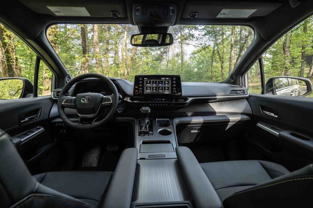 A view of the black front seats, steering wheel, dashboard, and touchscreen of a 2022 Toyota Sienna Woodland Special Edition minivan