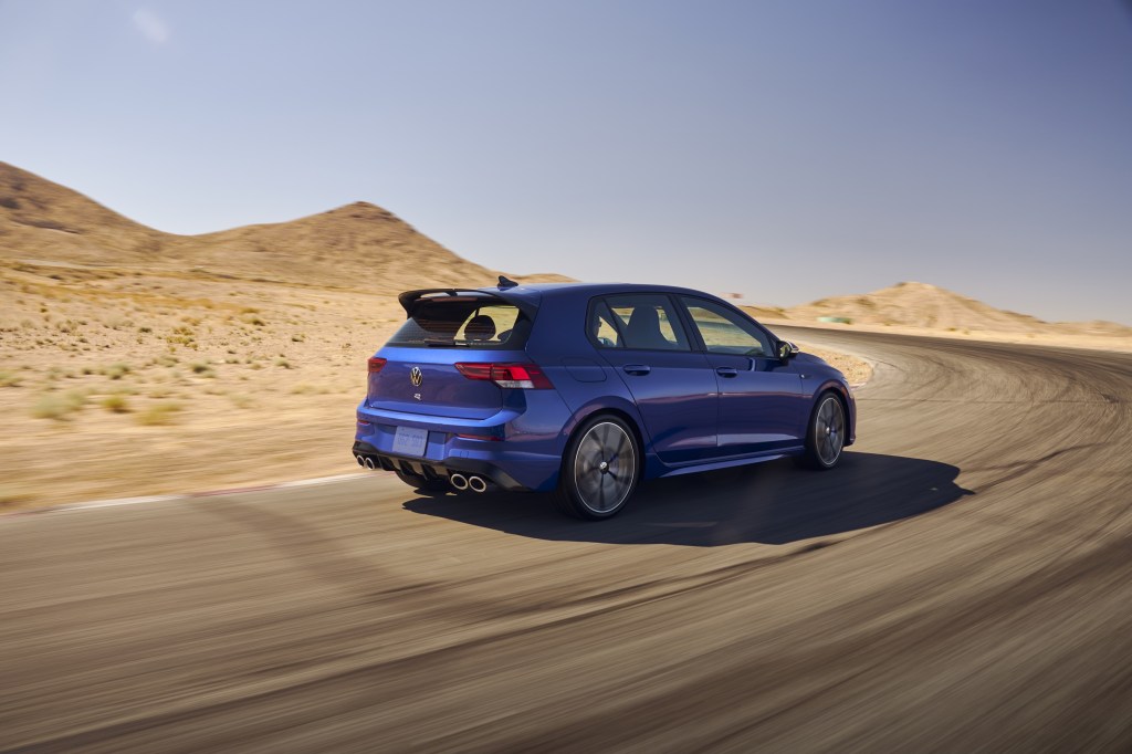 Passenger's side rear view of blue 2022 Volkswagen Golf R driving on a curvy road at speed
