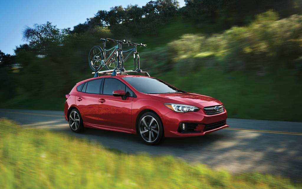 A red 2022 Subaru Impreza driving with bicycles on top. The Impreza is one of the cheapest cars you can buy.