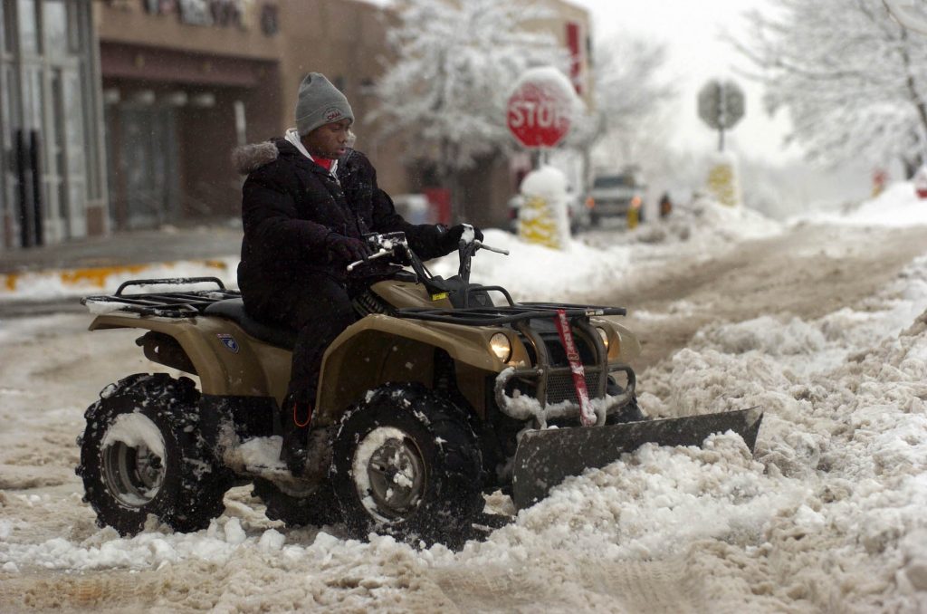 D'Rand Richardson uses a plow-fitted ATV to clear the parking lot in front of a Big Lots store in Louisville, Colorado
