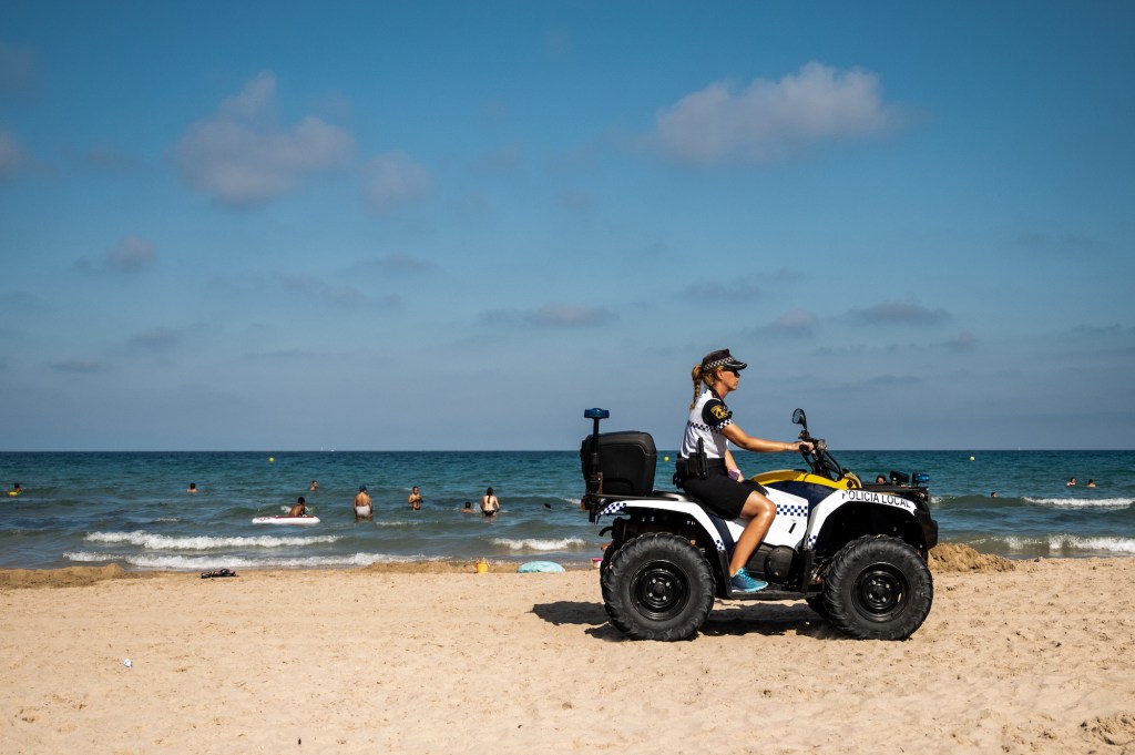 A police officer patrols on an ATV as tourists enjoy a day at the beach