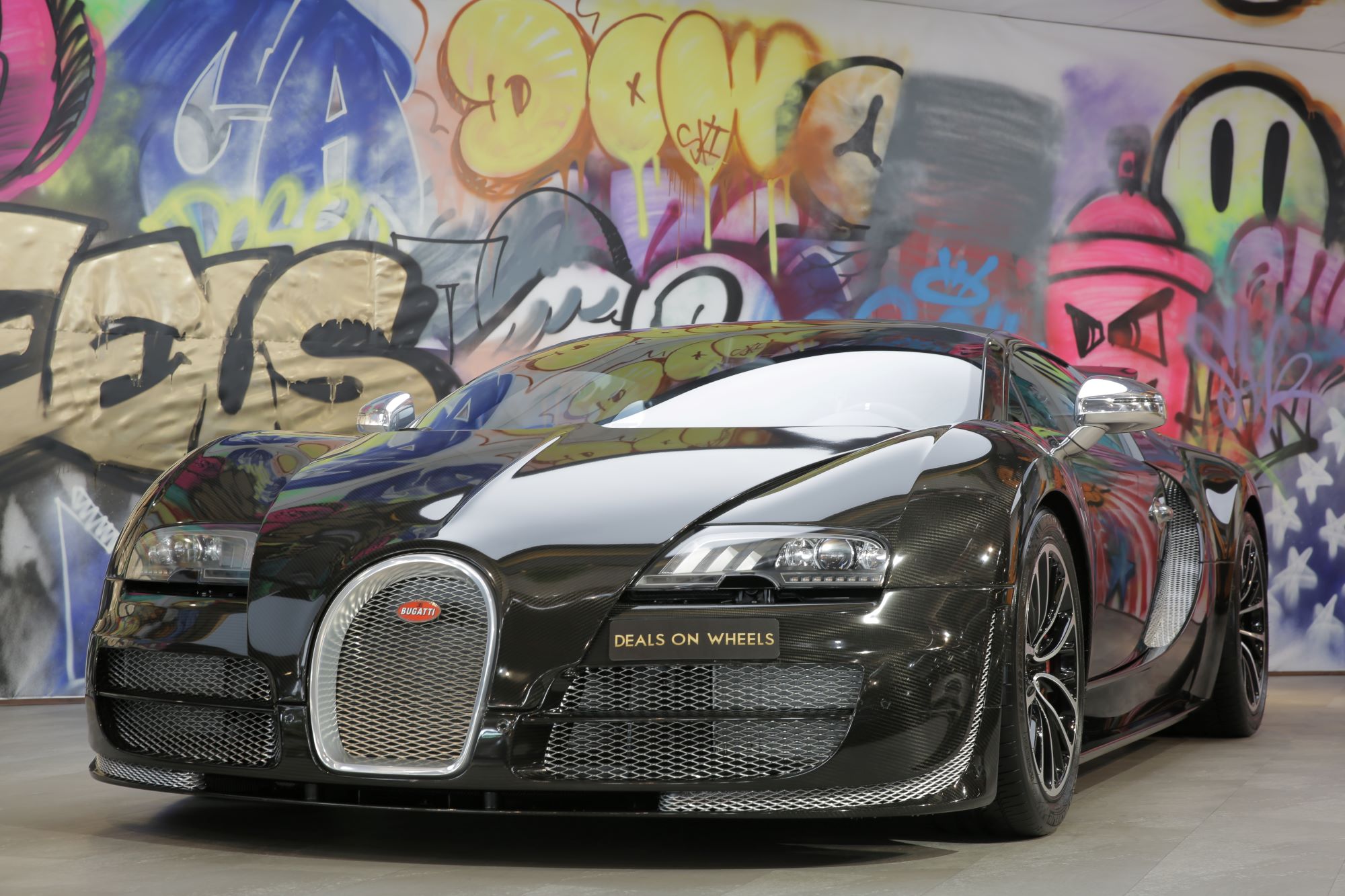 A black Bugatti Veyron Super Sport, the fastest car in the world, in front of a wall of graffiti.