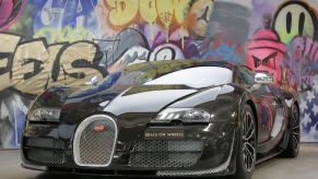 A black Bugatti Veyron Super Sport, the fastest car in the world, in front of a wall of graffiti.