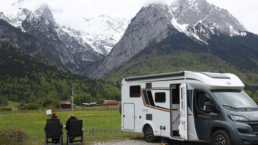 A camper van RV parked near mountains as a couple relaxes outside