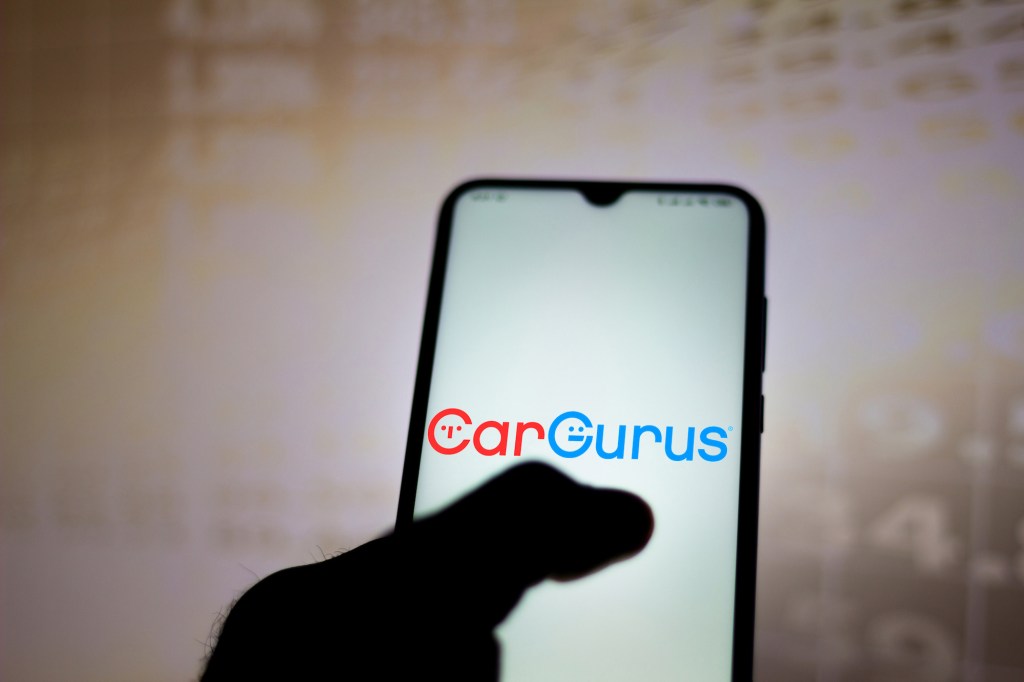 In this photo illustration, the CarGurus logo is displayed on a smartphone app