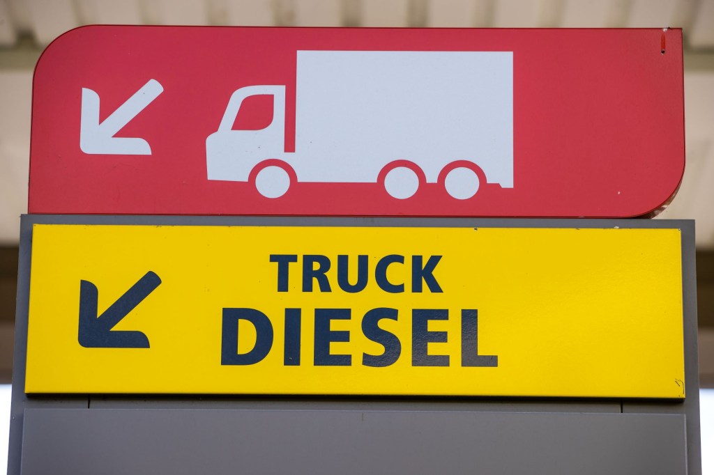A sign for truck diesel in yellow with black writing with a red sign above that with a white truck and trailer silhouette.