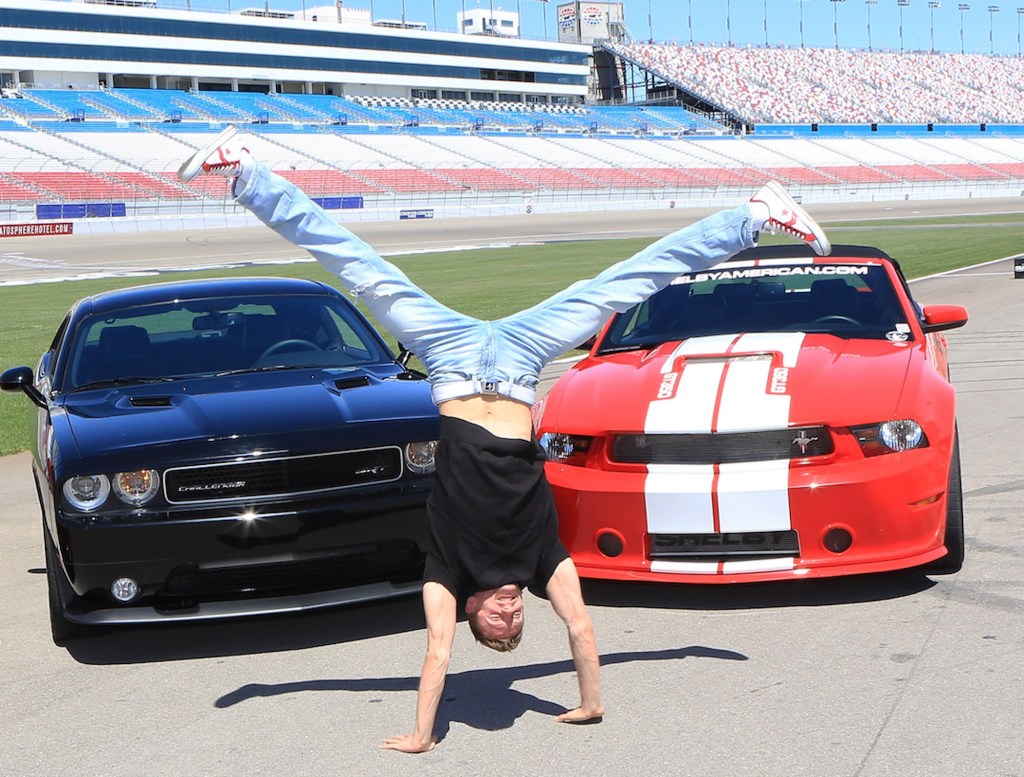 Misha Furmanczyk does a handstand in front of a Ford Mustang Shelby GT350 and Dodge Challenger SRT8 392 