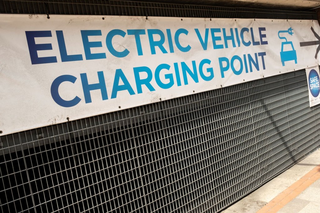 An 'Electric Vehicle Charging Point' sign tied to grating