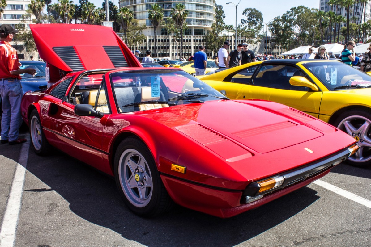 A red Ferrari 308 GTS at a car show with its engine cover open.