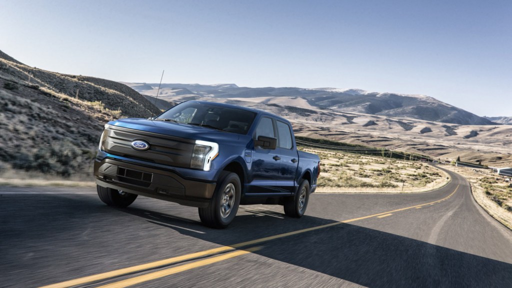 A blue 2022 Ford F-150 Lightning Pro Electric Truck driving down an empty street in the wilderness