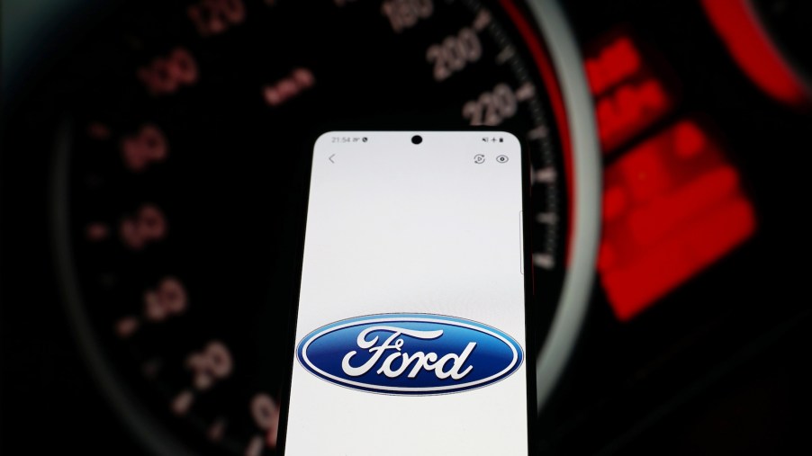 The Ford logo on a smartphone screen with a car's illumited instrumention panel in the background