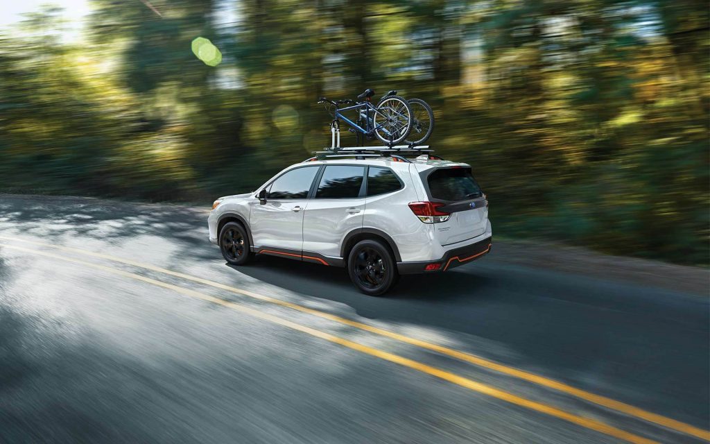 A white 2021 Subaru Forester driving down a tree-lined road. 